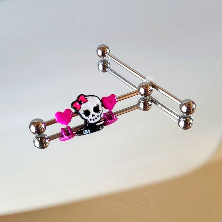 a pink and black skull with bow tie barbell ring sitting on top of a white surface