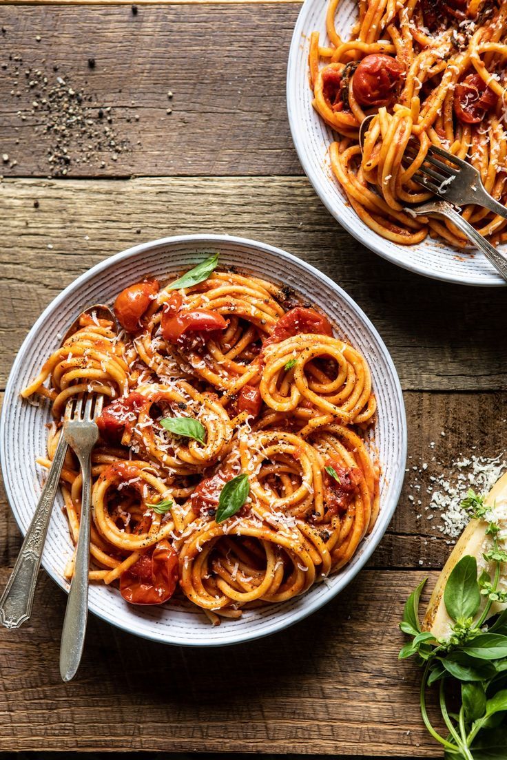 two plates of pasta with tomato sauce and parmesan cheese on the side next to a fork