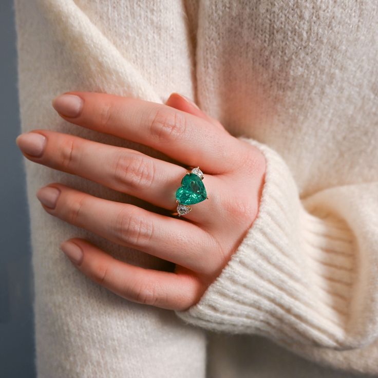 Sparkle with this one-of-a-kind statement ring featuring a 5.84 carat vibrant heart-shaped green emerald and 2 diamond side stones. This show-stopping ring will be sure to elevate any special occasion look. Available in 14K Yellow Gold Available in a size 7 Colombian emerald heart weight = 5.84 carats Diamond weight = 0.85 carats GIA certified This piece is one-of-a-kind and is FINAL SALE Fine Jewelry Green Heart Ring For May Birthstone, Fine Jewelry Green Heart Shaped Ring, Green Heart Ring For May Birthstone, Fine Jewelry Style, Luxury Green Heart Cut Rings, Green Heart Ring For May Birthstone, Green Heart-shaped Fine Jewelry Ring, Formal Green Heart Cut Rings, Heart-shaped Emerald Rings For Wedding, Elegant Emerald Heart Cut Rings