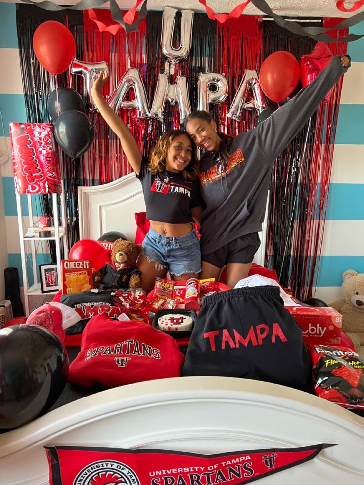 two women standing in front of a bed with red and black decorations