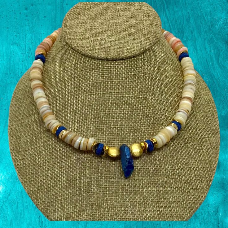 Experience the tropical vibes with our stunning 17" Fiji Choker Necklace of Lapis Lazuli, Gold, and beach-colored shells and beads. From the glint of gold to the mesmerizing blue of the Lapis Lazuli, this exquisite piece will make you feel like you've escaped to an island paradise! Toggle style closure. Unisexy! Artisan Beaded Necklace With Gemstone Beads For Beach, Adjustable Gold Beaded Shell Necklace, Gold Single Strand Beaded Necklace For Beach, Gold Natural Stones Jewelry For Vacation, Gold Jewelry With Natural Stones For Vacation, Bohemian Yellow Gold Single Strand Necklace, Beach Shell Necklace With Round Natural Stones, Ocean-inspired Gold Beaded Necklaces For The Beach, Ocean-inspired Gold Jewelry With Natural Stones