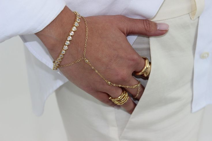 Ali Hand Chain - 18K Gold Plated, Brass, Cubic Zirconia Bracelet Length: 6in (includes 1in extender)  Cubic Zirconic: 2.5mm -CARE INSTRUCTION- Our jewelry is top-notch, but it needs a little TLC.  Check out these easy tips: - Keep it away from chlorine and salty water to dodge any tarnishing. -Spritz on your perfumes and lotions before putting on your bling to avoid a chemical clash. Hand Bracelet Gold, Gold Ring Bracelet, Gold Hand Chain, Hand Chain Bracelet, Bracelet Elegant, Cubic Zirconia Bracelet, Jewelry Minimalist, Hand Bracelet, Gold Hand