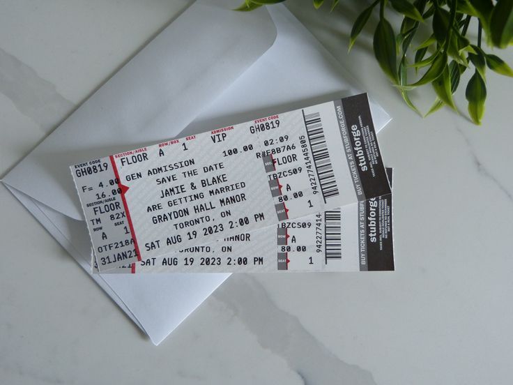 two tickets sitting next to each other on top of a white envelope with a plant in the background