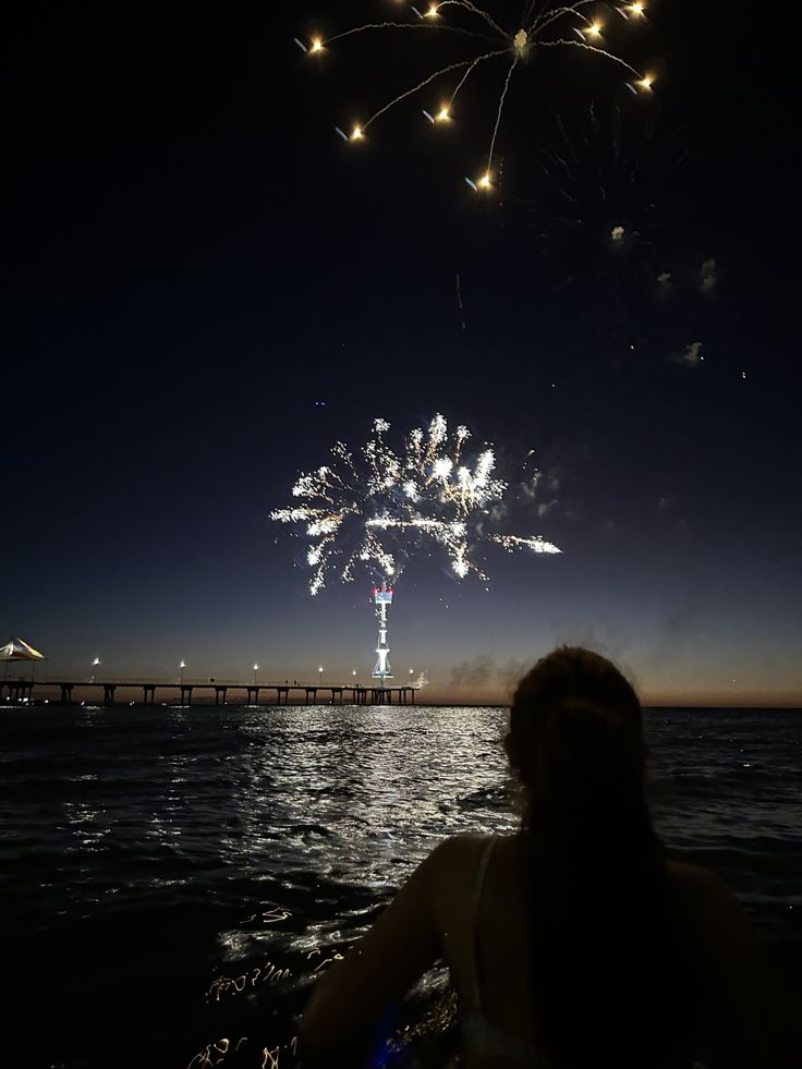 fireworks are lit up in the night sky over water with people watching from a boat