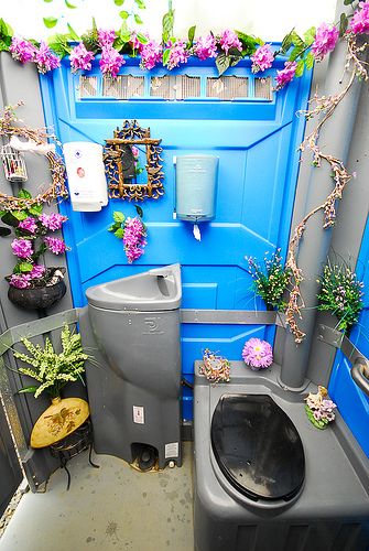 a bathroom with blue walls and purple flowers on the wall above the toilet is a trash can