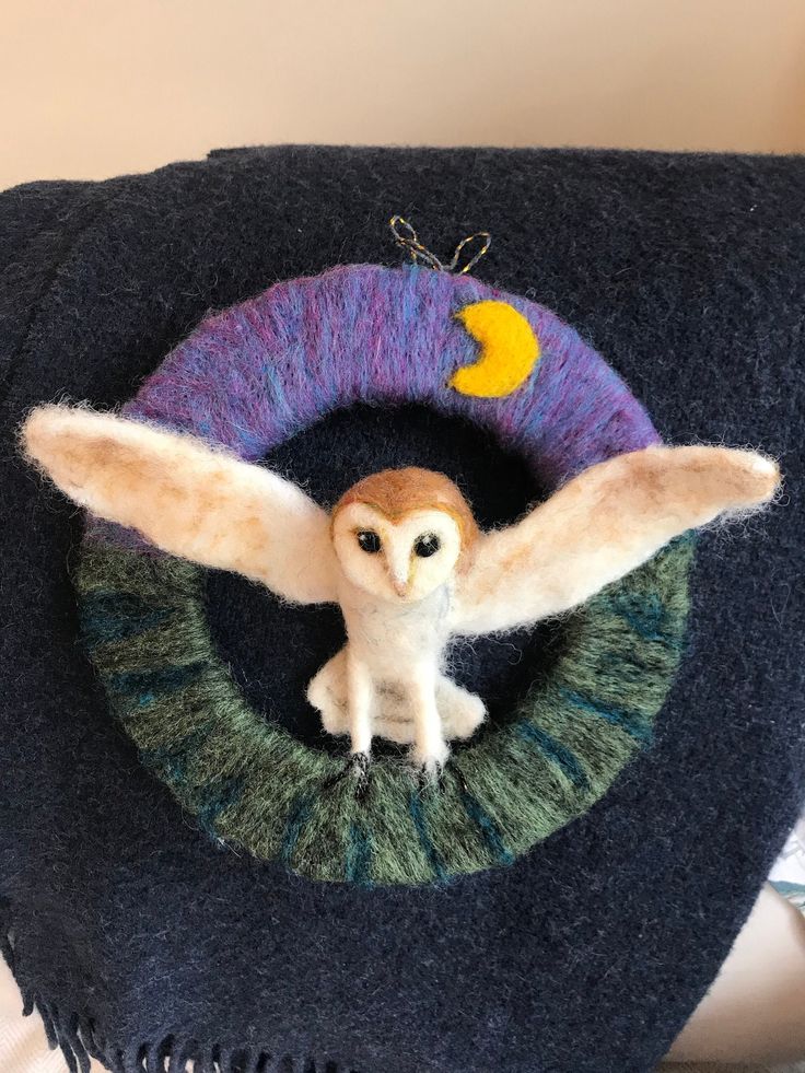 an owl figurine sitting on top of a blue and green blanket with a yellow moon hanging from it's center