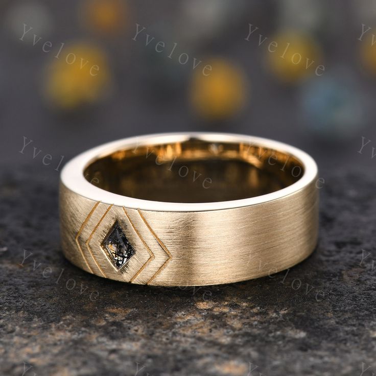 a yellow gold wedding band with a black diamond in the center on a granite surface