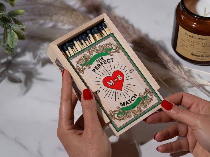 a person holding a match box with matches in it next to a candle and some feathers