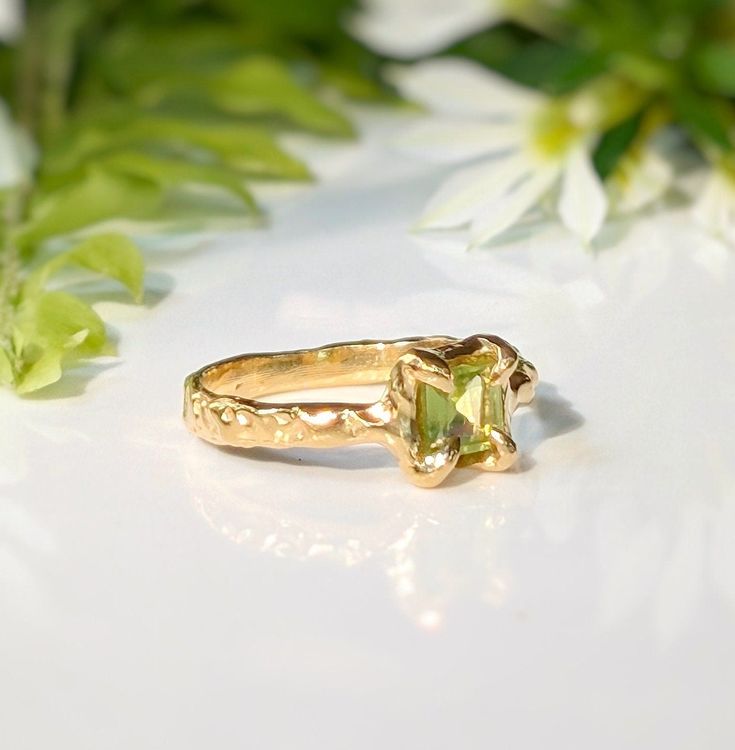 Show your love with this exquisite Peridot ring. Handcrafted in wax and cast in Solid 14k Gold, this stunning green crystal ring features an organic textured band, ensuring its uniqueness. Adorned with a mesmerizing princess-cut Peridot, also the August birthstone, it embodies more than an engagement ring - it symbolizes timeless love and individualityT H E ∙ S M A L L ∙ D E T A I L S• Princess-cut Peridot (5 x 5mm)• Solid 14k Gold textured bandM A T E R I A L ∙ O P T I O N S• Sterling Silver• S Organic Gold Engagement Ring, Peridot And Diamond Engagement Rings, Unique Peridot Jewelry For May Birthstone, Peridot Engagement Rings Gold, Unique Yellow Gold Jewelry For May Birthstone, Hand Forged Yellow Gold Nature-inspired Rings, Green Citrine Gemstone Rings, Nature-inspired Yellow Gold Ring Jewelry, Nature-inspired Yellow Gold Ring