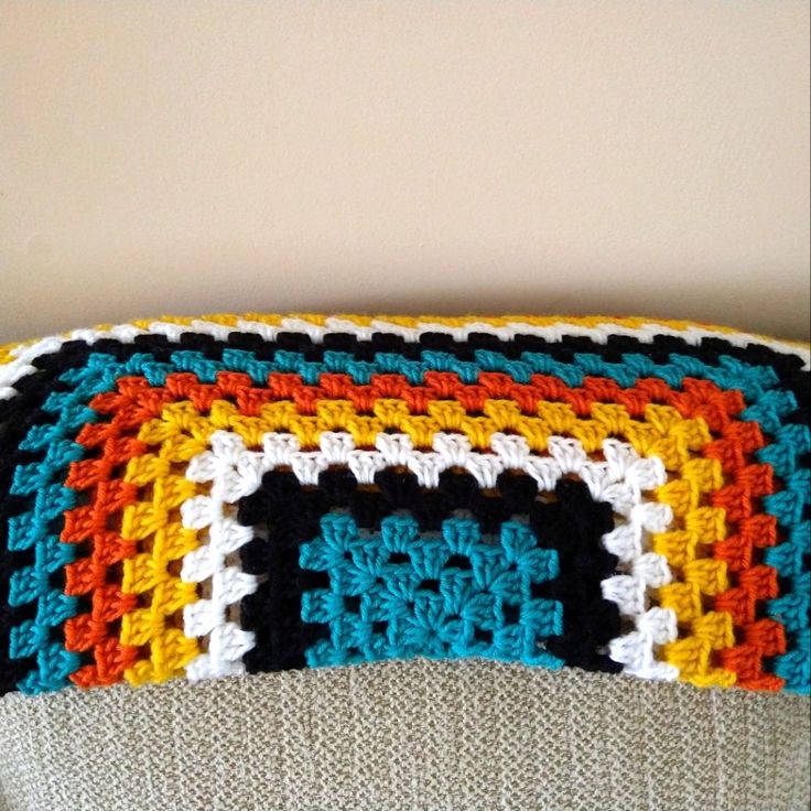 a crocheted granny blanket sitting on top of a couch next to a wall