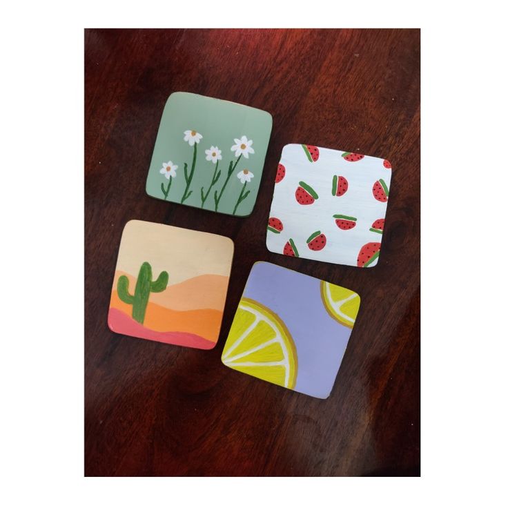 four square coasters with fruit designs on them sitting on a wooden table next to each other