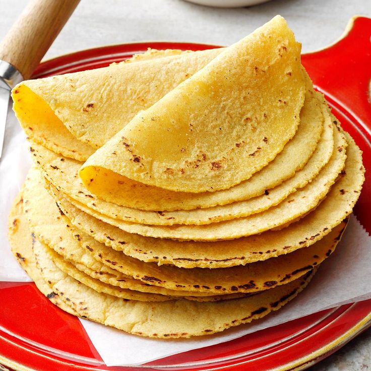 a stack of tortillas on a red and white plate with a wooden spoon