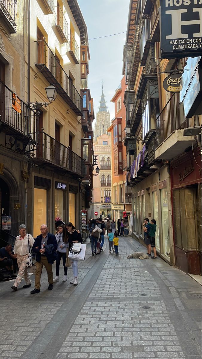 many people are walking down the street in an old european city with tall buildings and balconies