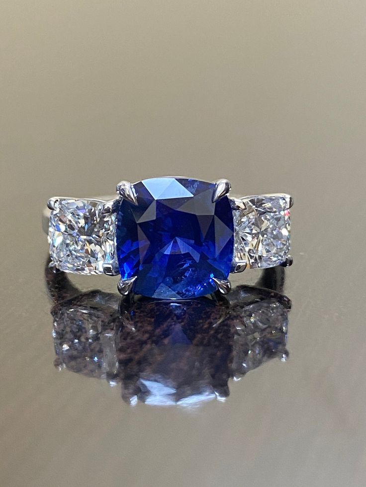 "DeKara Designs Collection Beautiful Modern/Art Deco Ceylon Blue Sapphire and Diamond Ring Metal- 90% Platinum, 10% Iridium Stones- Genuine Ceylon Cushion Cut Blue Sapphire 4.14 Carats. Two GIA Certified Cushion Cut Diamonds E Color VS2 0.92 Carats, F Color SI1 Clarity 0.95 Carats. Ring Comes With Sapphire Certificate and GIA Diamond Certificates. Size-7. FREE SIZING Entirely Handmade, Classic and Timeless Art Deco Inspired Ceylon Blue Sapphire Three Stone Cushion Cut Diamond Engagement Ring. Th Blue Sapphire Ring With Diamond Cut Asscher Shape, Gia Certified Blue Sapphire Ring In Platinum, Blue Asscher Cut Diamond Sapphire Ring, Cushion Cut Blue Sapphire Rings, Blue Asscher Cut Sapphire Ring With Diamond Details, Blue Asscher Cut Sapphire Ring With Diamond Cut, Blue Cushion Cut Lab-created Sapphire Rings, Luxury Blue Diamond Anniversary Ring, Sapphire Rings With Diamond Cushion Cut