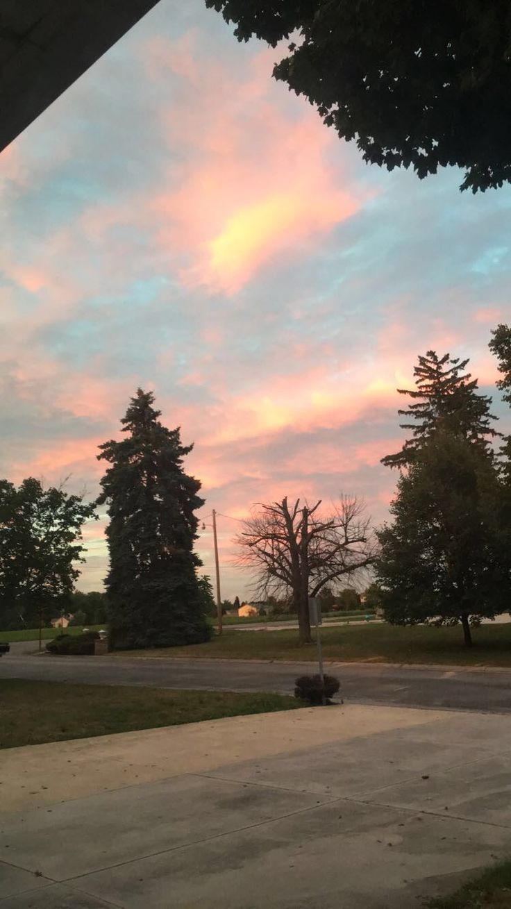 the sky is pink and blue with clouds in front of some trees on either side