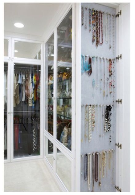 a closet filled with lots of necklaces and bracelets hanging on the wall next to glass doors