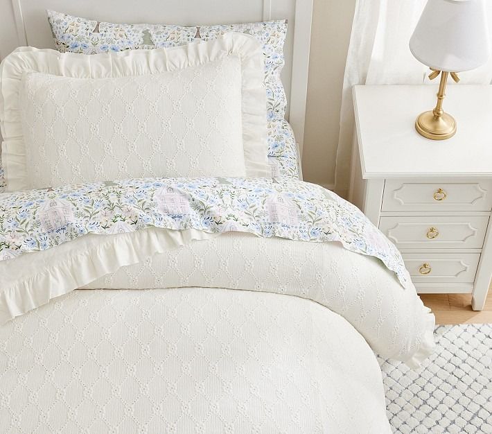 a bed with white comforter and pillows next to a lamp on a nightstand in a bedroom