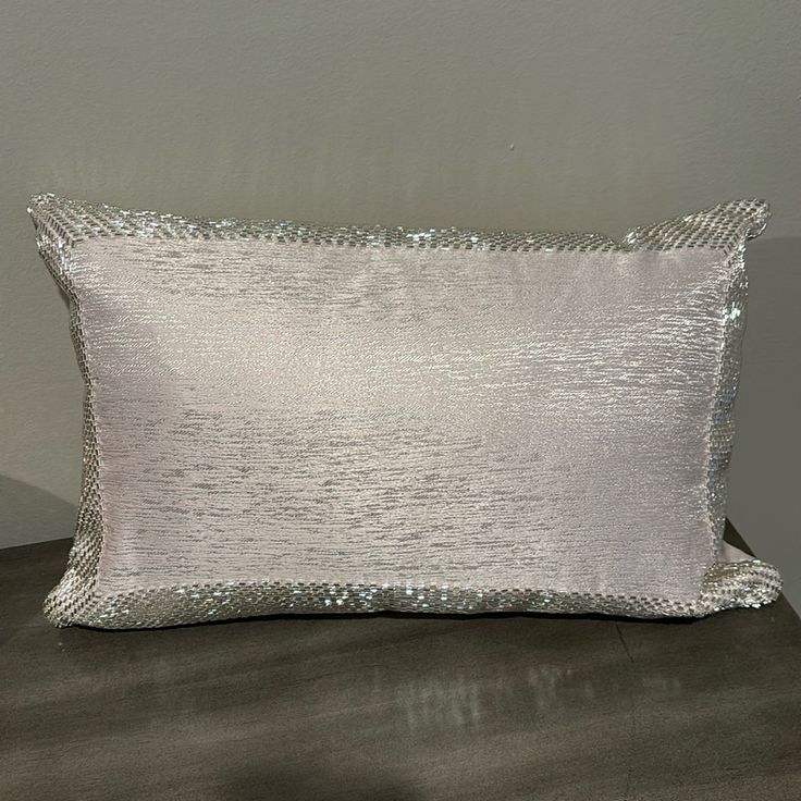 a white pillow with silver sequins on it sitting on a table next to a gray wall