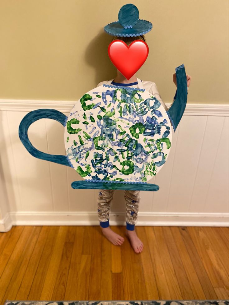 a young boy is holding up a teapot shaped like a person with a heart on his head