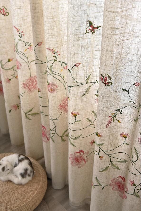 a cat laying on top of a rug next to a window covered in curtains with flowers