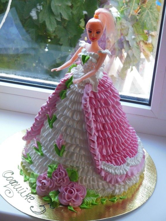 a barbie doll cake sitting in front of a window