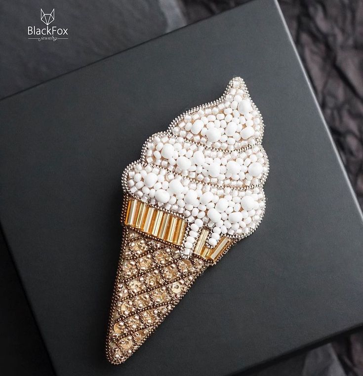 an ice cream cone brooch sits on a black box with pearls and gold trim