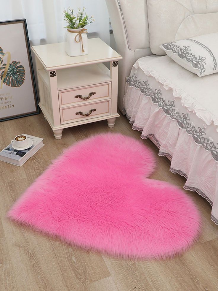 a pink heart shaped rug sitting on top of a wooden floor next to a bed