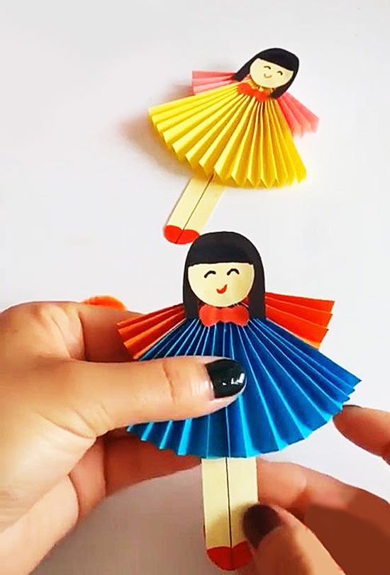 a hand holding a paper doll next to a flower