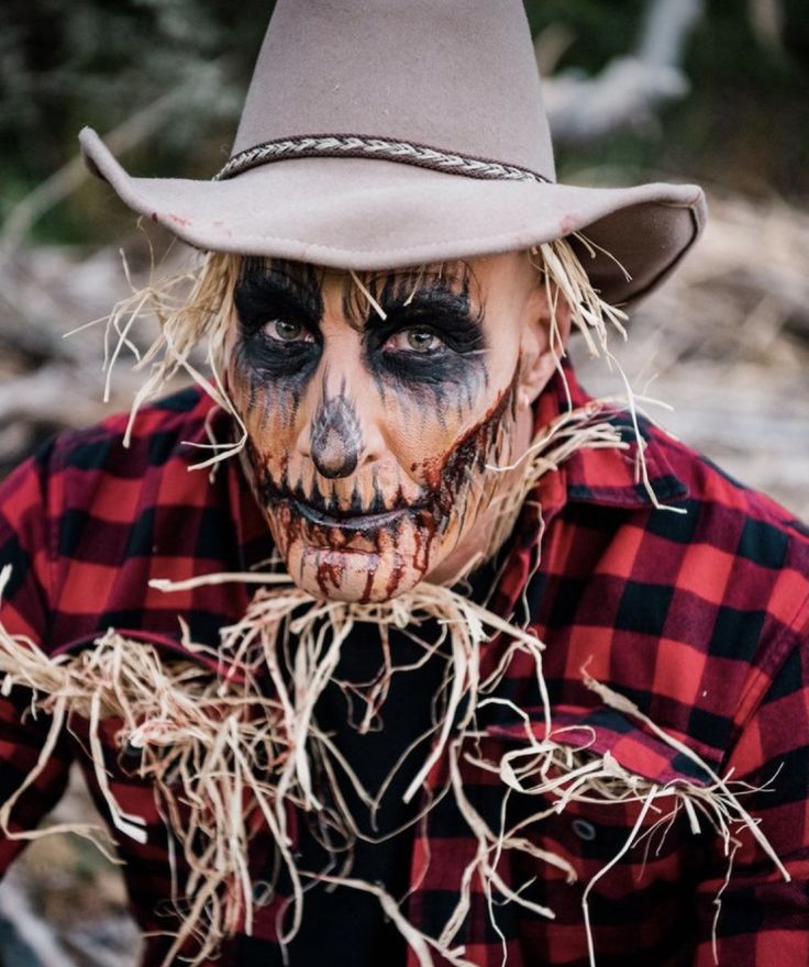 a man with makeup on his face wearing a cowboy hat and holding hay in front of his face