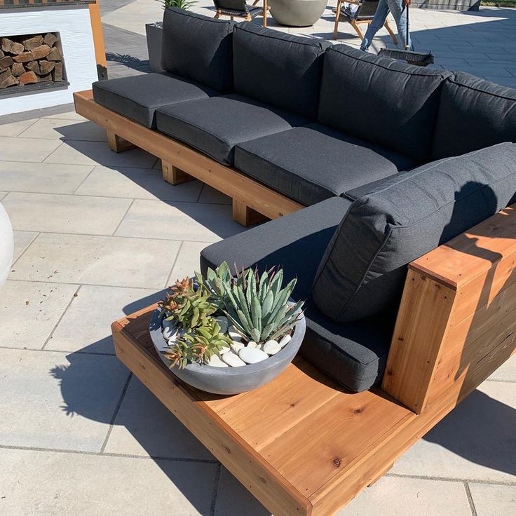 a couch and table on a patio with potted plants in the center, next to a fire pit