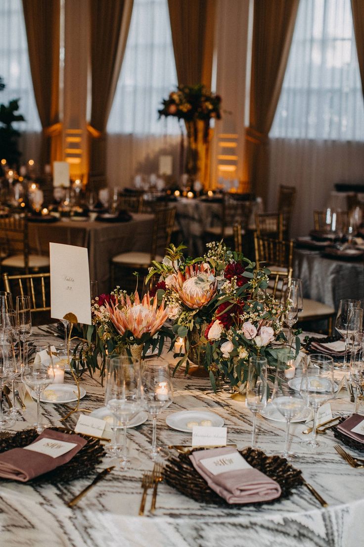 the table is set with wine glasses, place settings and flowers in vases on it