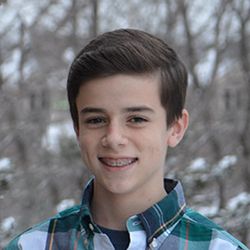 a young boy is smiling for the camera in front of some snow covered trees and bushes