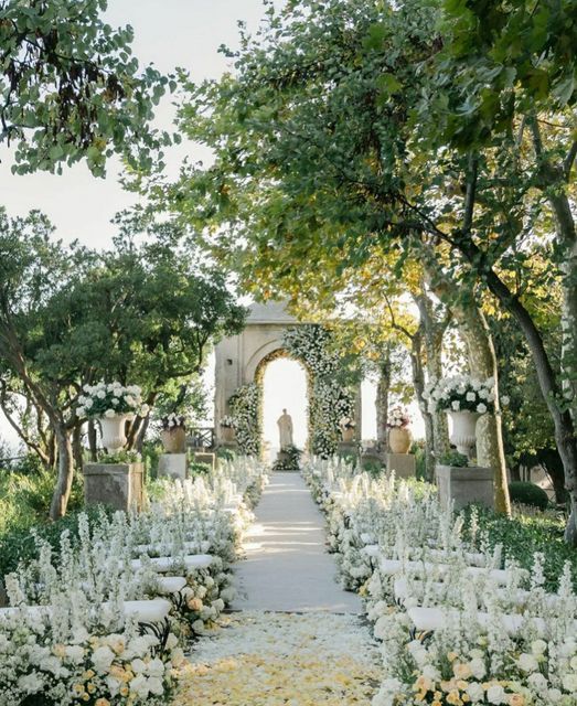 an outdoor wedding ceremony with white flowers and greenery on the aisle, surrounded by trees