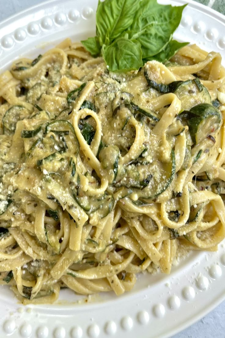 a white plate topped with pasta covered in sauce and spinach leaf garnish