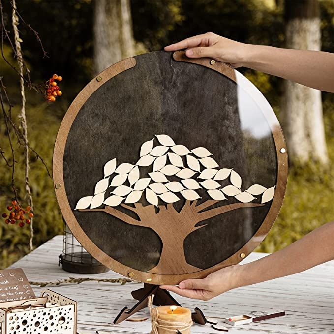 a person holding up a wooden plate with a tree painted on it and other items around it