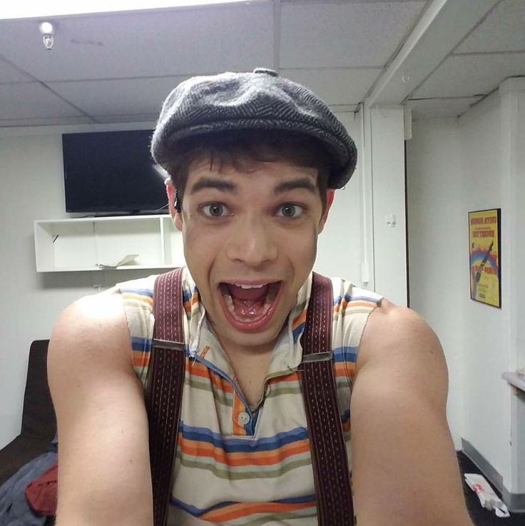 a man with suspenders and a hat on taking a selfie