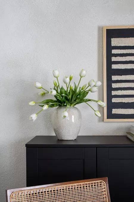 a vase with white flowers sitting on top of a black cabinet