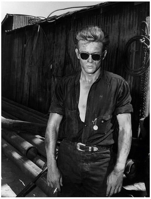 black and white photograph of a man in sunglasses standing next to a fence holding a baseball bat