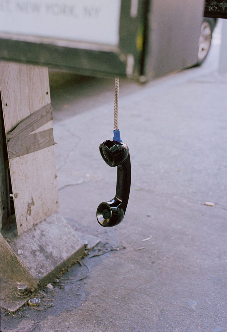 an old phone hanging from a rope on the side of a street next to a truck