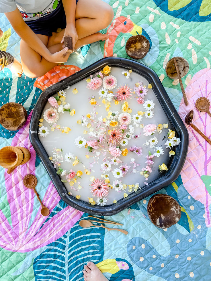 a woman is sitting on the ground with flowers in a tray full of water and spoons