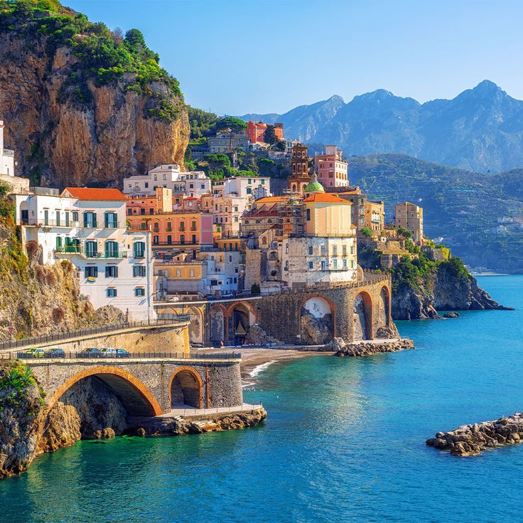 an old bridge over the water in front of some buildings with mountains in the background