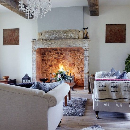 a living room filled with furniture and a fire place under a chandelier in front of a stone fireplace