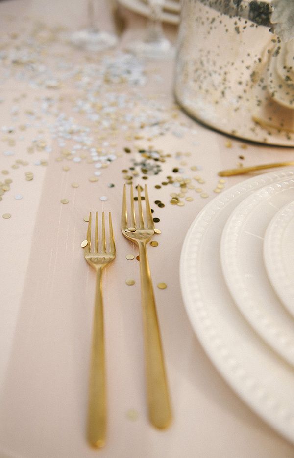 the table is set with white plates and gold cutlery, confetti and silverware