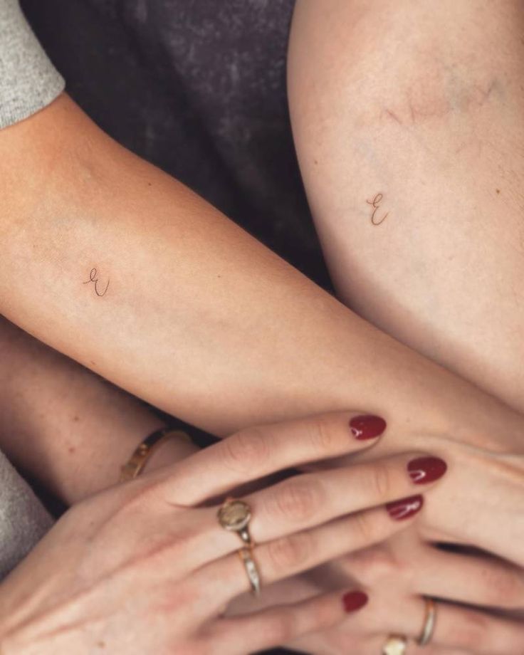 two women with matching tattoos on their arms, one holding the other's arm