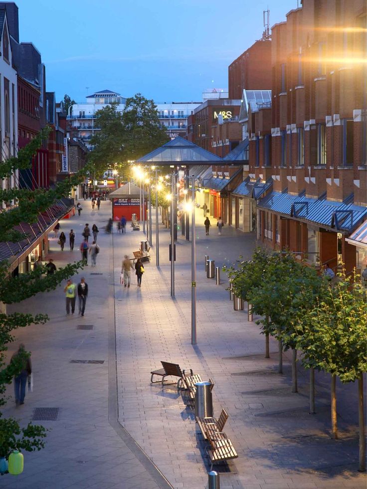 people are walking down the street at night in an urban area with trees and benches