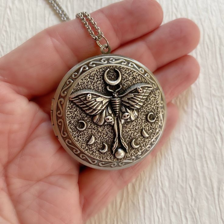 "This gorgeous antiqued silver locket features a luna moth and will become a special addition to your jewelry collection. The locket is extra large at 46mm in diameter and opens for a secret place to keep pictures, messages, or whatever you like. The inside of this locket is deep and can hold two photos. The inside space is approximately 30mm in diameter. The locket is made from lightweight silver plated brass. It has been deeply embossed with an intricate pattern and has a beautiful luna moth o Moth Necklace, Large Locket, Jewelry Knowledge, Necklace Locket, Secret Place, Witchy Crafts, Silver Locket, Luna Moth, Photo Locket