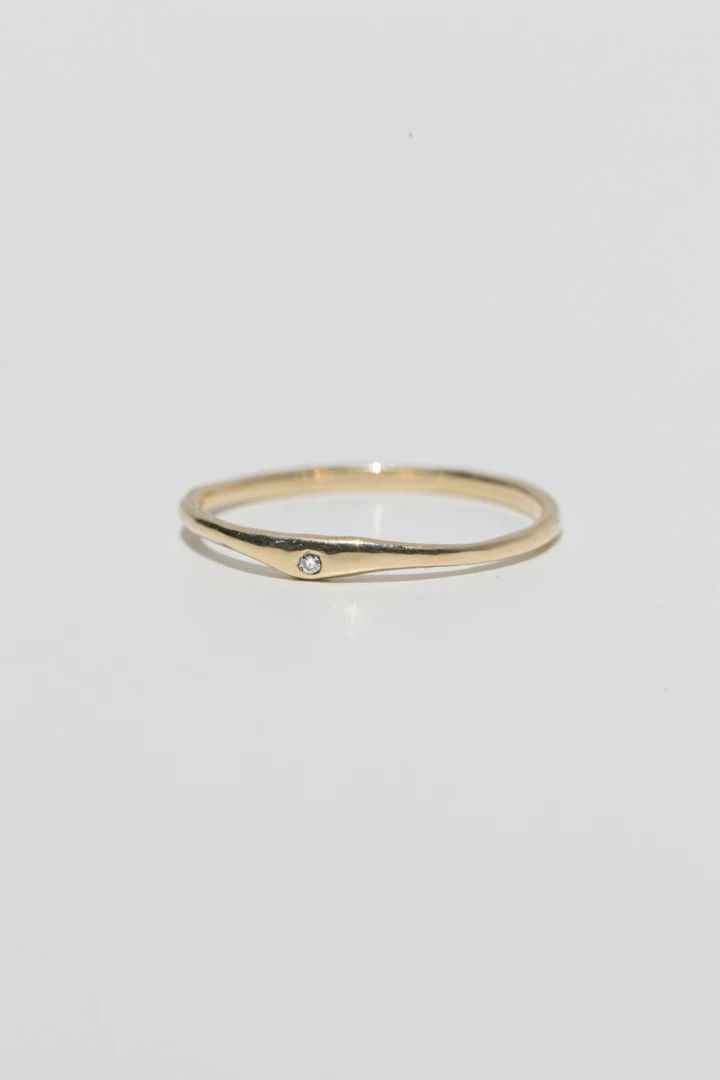 a gold ring with a single diamond on the top and bottom, sitting on a white surface