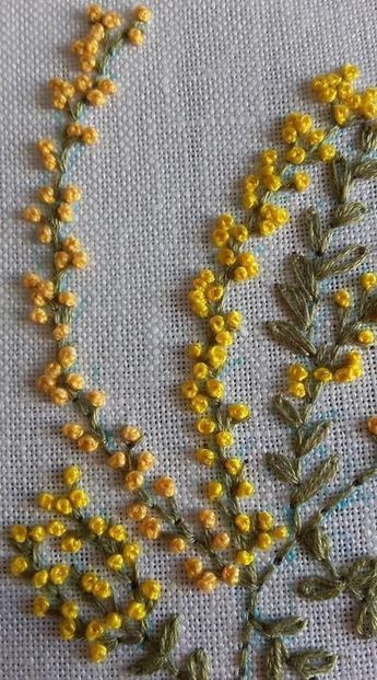 some yellow flowers are sitting on a white cloth with green stems in the middle and one flower has been embroidered onto it