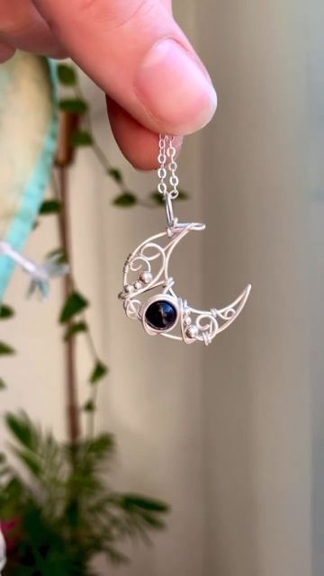 a hand holding a silver necklace with an evil moon and eye hanging from it's side