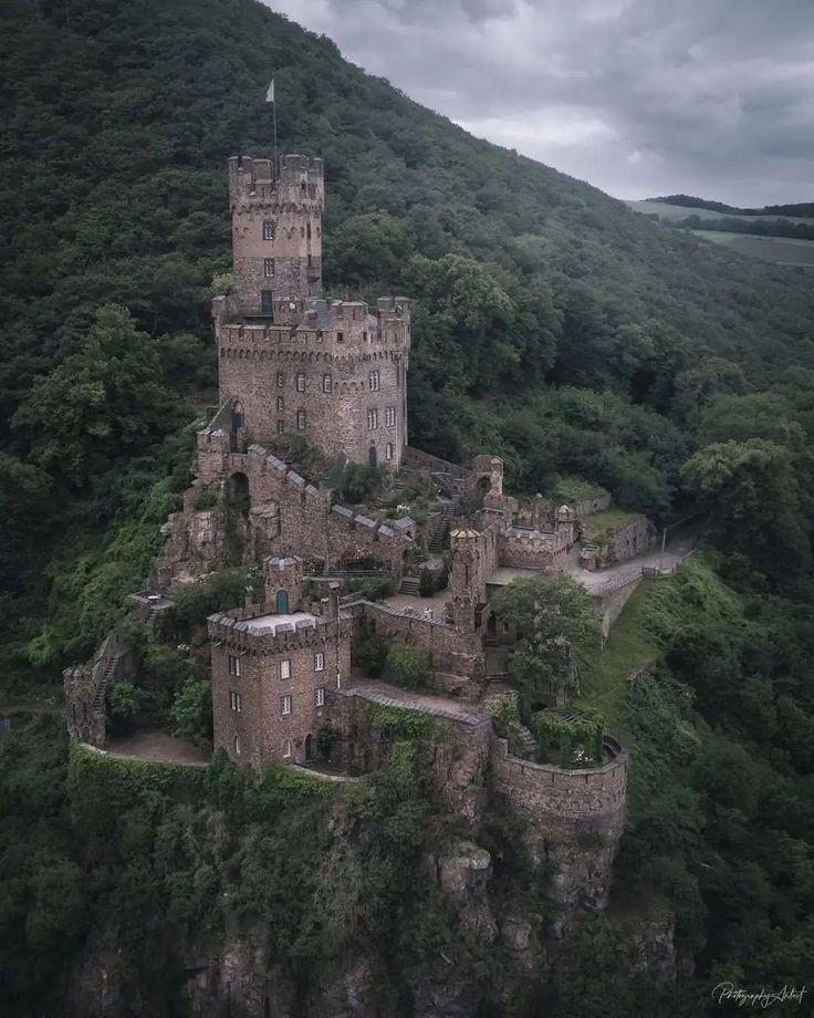 an old castle perched on top of a cliff in the middle of a green forest